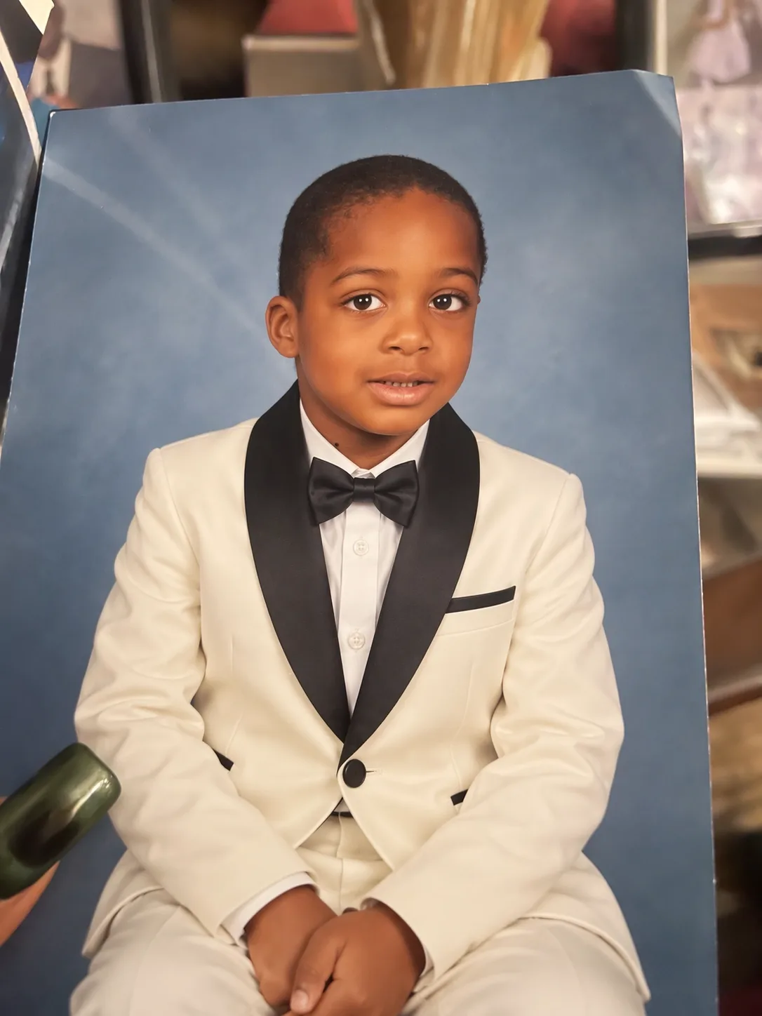 The same photo edited with Images 2.5: the boy now wears a white tuxedo and black bow tie, while the hand and background are unchanged.