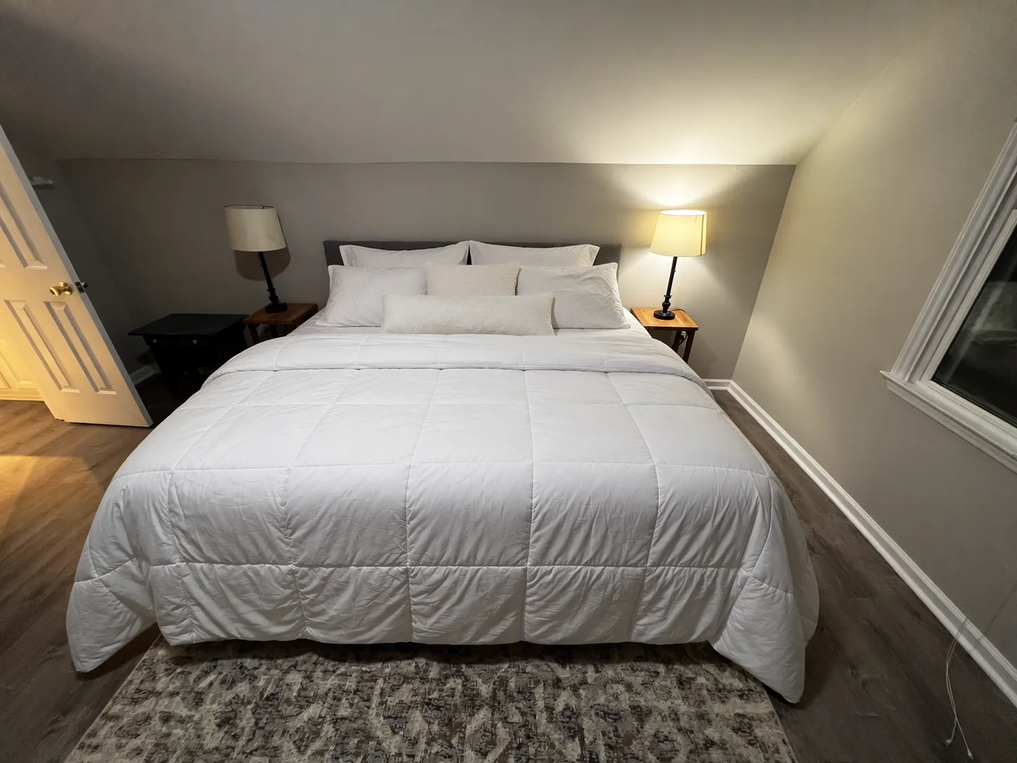 The same room with the bed neatly made; walls, lamps, rug and floor are unchanged.